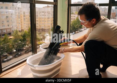 Professional HVAC technician wearing safety glasses using steam cleaner to clean air conditioner filter in bucket of water, performing maintenance on Stock Photo