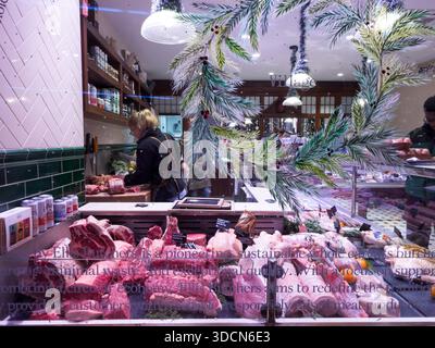 London, England – Butcher shop staff with Christmas decorated chilled meat display counter, festive food retail and seasonal provisions Stock Photo