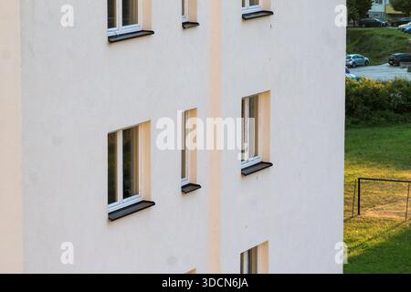 Minimalist residential building exterior with a white plaster facade and rectangular windows, captured in warm evening light. Clean lines and modern. Stock Photo