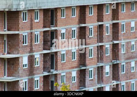 Residential apartment building exterior under construction, featuring exposed brick facade, repetitive windows, and raw concrete floors. Stock Photo
