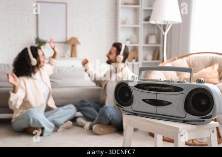Boombox on stool against couple in headphones listening to radio at home, closeup Stock Photo
