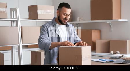 Male seller packing parcel for client at table in warehouse Stock Photo ...