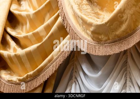 Elegant gold fabrics featuring striped and damask patterns, layered with fringe trim. Perfect for upscale decor, curtains or background textures. Warm Stock Photo