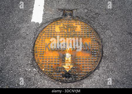 Kuantan, Malaysia - November 23, 2025 - Rusty cast iron manhole cover marked "KUMBAHAN" (Drainage or Sewerage) embedded in asphalt in Malaysia Stock Photo