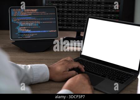 Close up of hands typing on a laptop at an office desk with a blank screen mockup and copy space, programming code and data analysis setup in the back Stock Photo