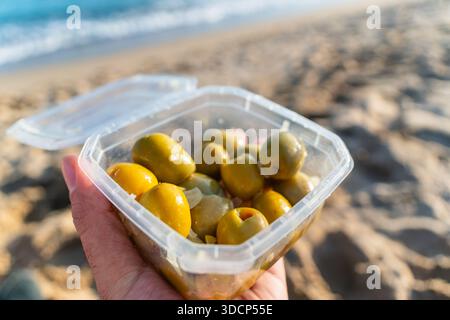Green olives inside box in hand on the beach in Barcelona Stock Photo