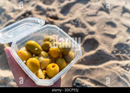 Green olives inside box in hand on the beach in Barcelona Stock Photo