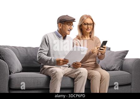 Senior couple sitting on a sofa and using a smartphone and documents isolated on white background Stock Photo