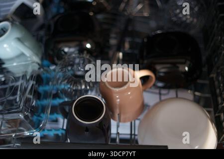 close-up view of various inverted ceramic mugs and glass dishes arranged in the top rack of a dishwasher, featuring a blend of muted colors and gentle Stock Photo