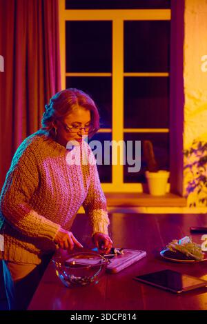Senior woman cooking while interacting with virtual assistant interface Stock Photo