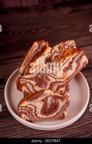 close-up of marble cake slices showcasing intricate swirls of chocolate and vanilla, artistically arranged on a white ceramic plate against a dark, te Stock Photo
