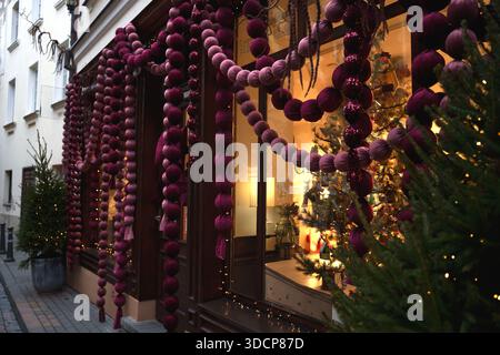 vibrant holiday display featuring rich purple garlands and festive tree in illuminated street setting with cozy interior view through glass window, se Stock Photo