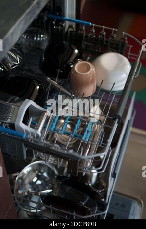 open dishwasher with an assortment of clean dishes, glassware, and utensils in a modern kitchen setting, highlighting a play of shadows and subtle col Stock Photo