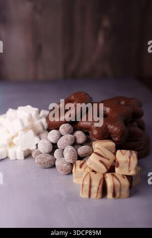 assorted holiday cookies and confections on textured surface with dark wooden background, featuring chocolates, sugar-coated delights, marshmallow sha Stock Photo