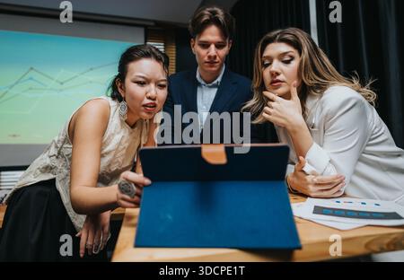 Three colleagues review data on a laptop during a focused business meeting in a conference room Stock Photo