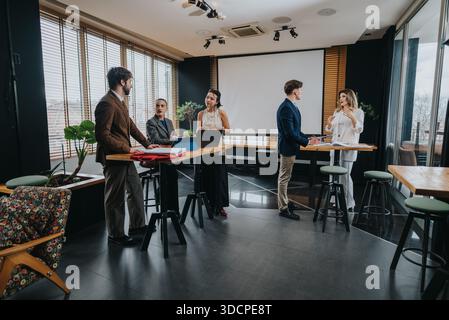 Business coworkers collaborate in a bright, modern office, discussing projects and ideas at standing tables with laptops Stock Photo