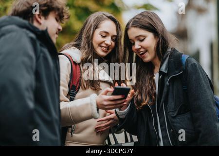 Teen friends look at smartphone together outdoors, smiling and sharing a moment Stock Photo