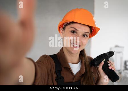 Woman Builder. Female construction worker making selfie with drill on mobile phone. Technology, repair, construction and building concept. copy space Stock Photo