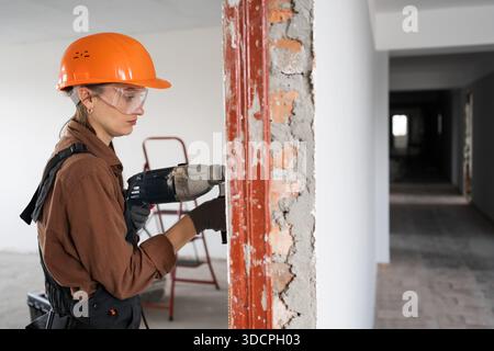 Female construction worker using hammer drill. Builder woman with pneumatic hammer drill perforator making hole in wall. copy space Stock Photo
