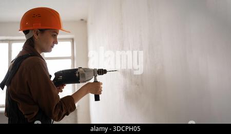 Female construction worker using hammer drill. Builder woman with pneumatic hammer drill perforator making hole in wall. banner. copy space Stock Photo