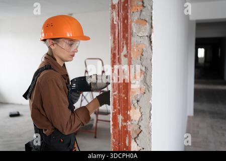 Female construction worker using hammer drill. Builder woman with pneumatic hammer drill perforator making hole in wall. copy space Stock Photo