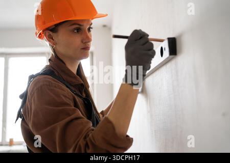 Female Construction worker in hardhat measuring concrete wall using spirit level during home renovation work. copy space Stock Photo