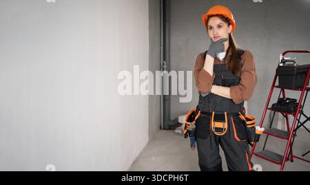Woman Builder. Pensive female Architect in work overalls and hardhat thinking new idea in unfinished building. repair, construction and building conce Stock Photo