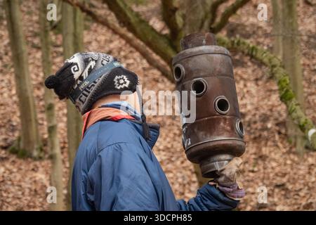 Young cout holding a rusty metal heating unit in a forest, wearing winter clothing during an outdoor activity in woodland setting Stock Photo