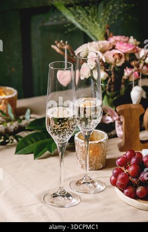 st. Valentines day or wedding romantic table setting with wooden letters love, needle felted hearts, bouquet of pink roses, couple glasses of champagne and red grapes on natural linen tablecloth. Stock Photo