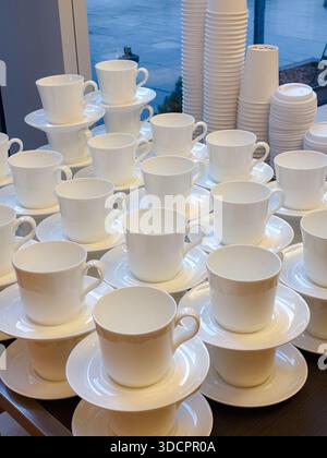Stacks of clean white ceramic coffee cups and saucers, ready for service in a hotel or hospitality setting. Stock Photo