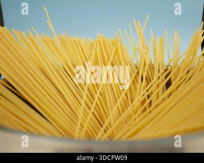Closeup top edge view of uncooked spaghetti fanned out inside metal pot on blue background, detailed texture of long dry pasta for Italian food concep Stock Photo