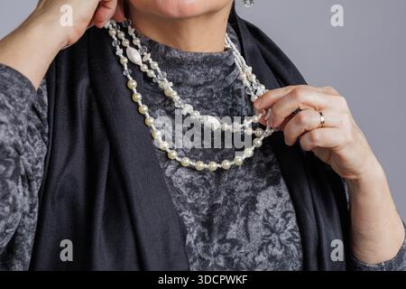 Close-up of hands adjusting a layered pearl necklace against a textured outfit. Stock Photo