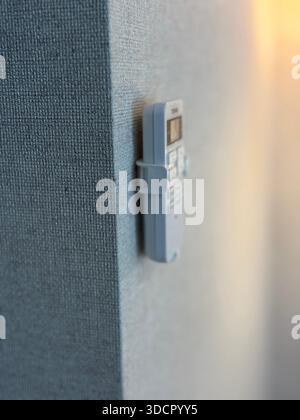 Remote control mounted on textured wall with soft light in background offering a modern aesthetic. Mobile photo Stock Photo