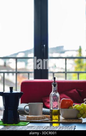 Close-up vertical shot of a healthy Mediterranean-style breakfast on a coffee table. Moka coffee pot, bread, olive oil, bowl with grapes and persimmon Stock Photo