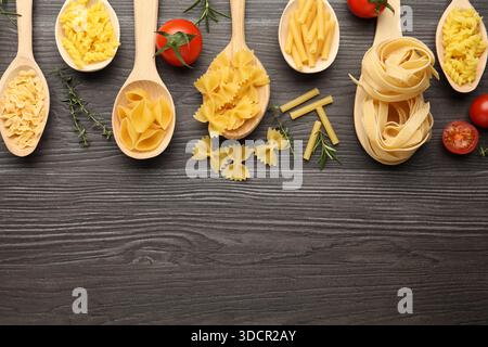 Different types of raw pasta in spoons, tomatoes, rosemary and thyme on wooden table, flat lay. Space for text Stock Photo
