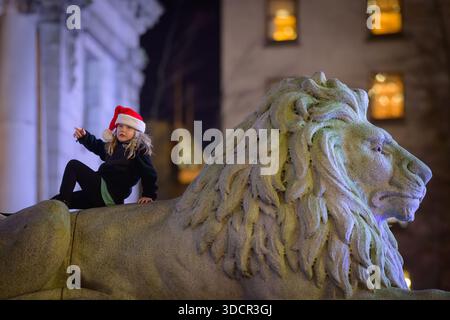 Child with Santa hat playing on stone lion. Stock Photo