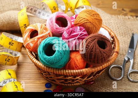 Balls of yarns, buttons, scissors, measuring tape and burlap fabric on wooden table, closeup Stock Photo