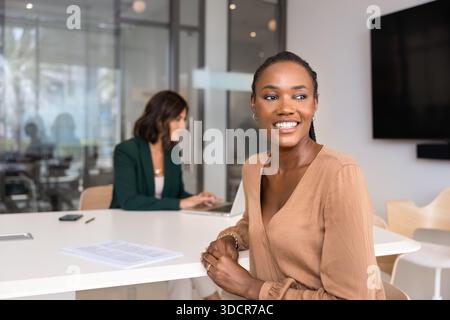 Happy dreamy young African American businesswoman sitting at meeting table Stock Photo