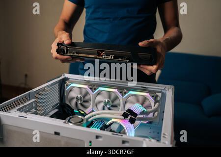 Computer technician installing powerful new graphic card into custom-built gaming pc, featuring vibrant RGB lighting and advanced water cooling system Stock Photo
