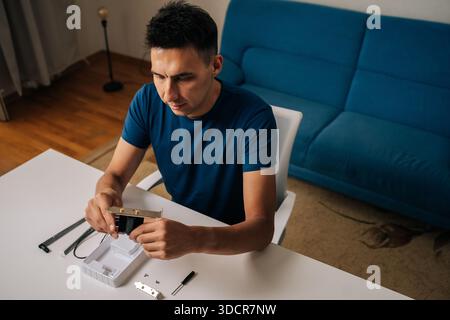 High-angle view of technician male assembling wi-fi module using tools at home office desk, focusing on intricate components and ensuring proper Stock Photo