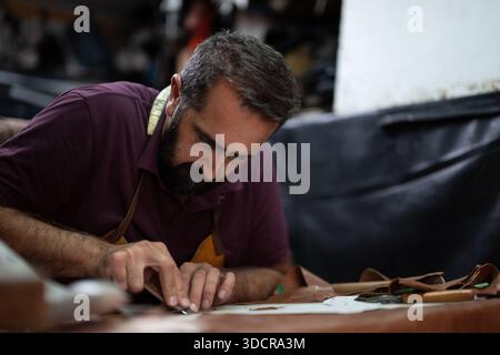 A skilled craftsman with a beard focuses on leather cutting at a workshop Stock Photo