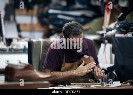 Skilled craftsman works on a leather shoe in a busy workshop, focused on handcrafting Stock Photo