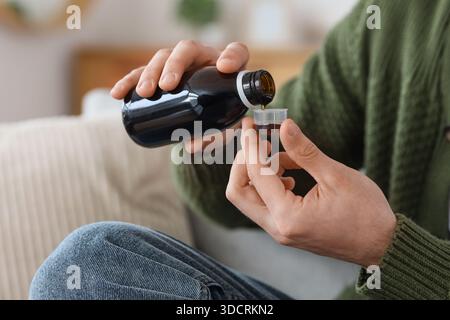 Young man pouring cough syrup from bottle into measuring cup at home, closeup Stock Photo
