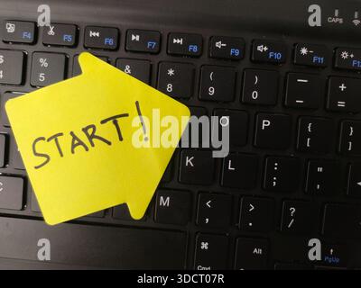 The image features a yellow sticky note with the handwritten word START placed prominently on a black computer keyboard. Stock Photo