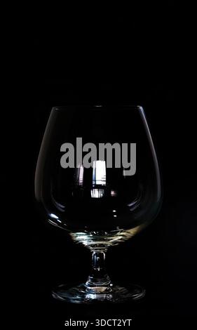 A dramatic and minimalist studio photograph featuring an elegant empty brandy snifter or cognac glass isolated against a solid black background. Low k Stock Photo