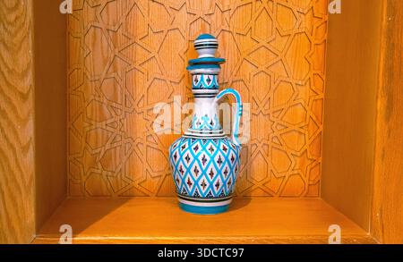An elegant pitcher adorned with blue and white geometric patterns rests in a carved wooden niche, showcasing craftsmanship and traditional aesthetics. Stock Photo