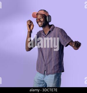 Happy young Black man dancing while listening to music with wireless headphones in a studio setting. Relaxed lifestyle, joy, freedom and modern music Stock Photo
