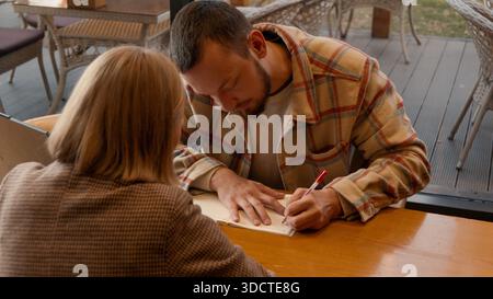 Man and woman writing on paper and studying together in cafe. Stock Photo