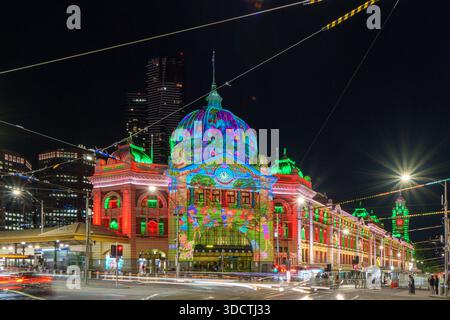 Flinders Street Station is illuminated with colorful festive projections and lights at night, with blurred car light trails on the street. Stock Photo