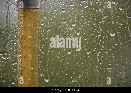 Close-up shot of raindrops on a glass pane, alongside a yellow pole, creating a serene and tranquil atmosphere. Stock Photo